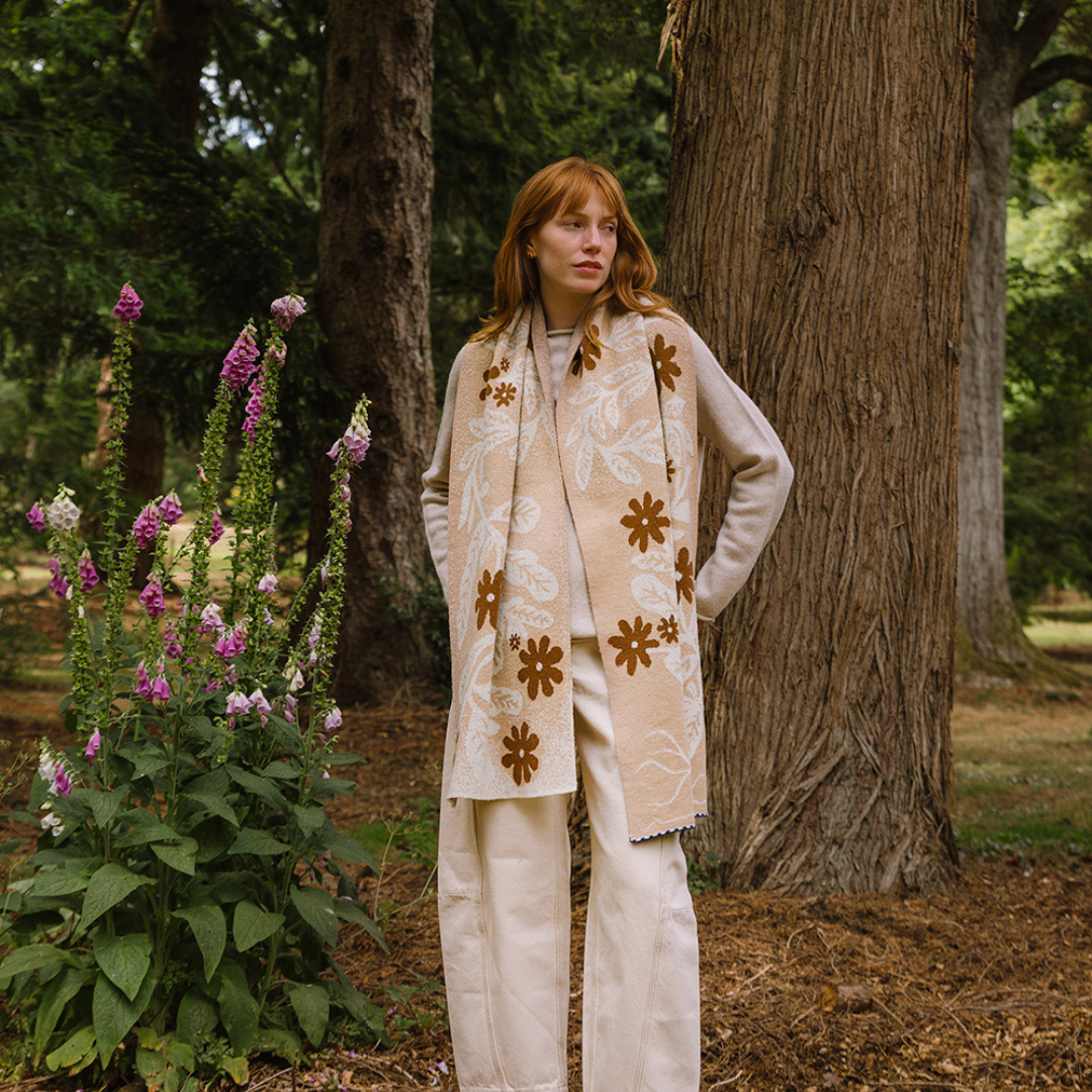 Person wearing a floral scarf in a natural setting with trees and flowers.