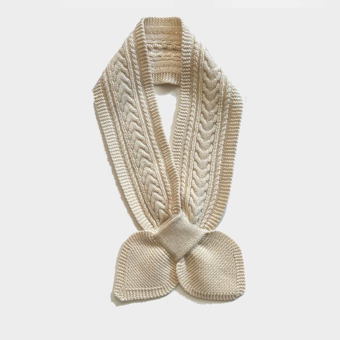 A cream-colored cable-knit scarf with a knotted bow at the bottom, displayed against a light gray background.
