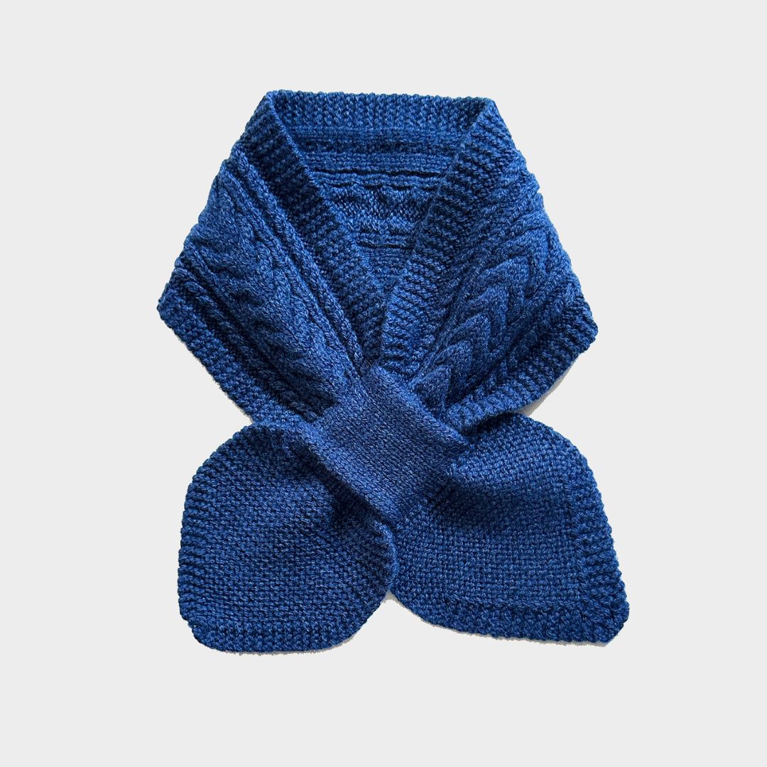 A royal blue cable-knit scarf folded and tied in a bow shape, displayed against a light gray background.