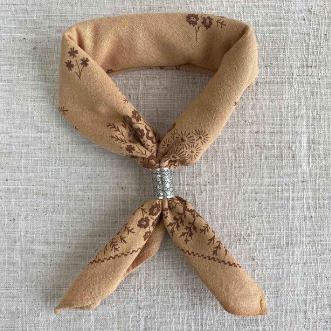 a brown neckerchief with a sliver slider on a grey background.