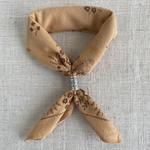 a brown neckerchief with a sliver slider on a grey background.