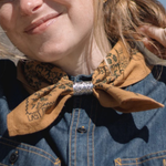 Close-up of a person wearing a denim jacket with a decorative brown scarf and slider..