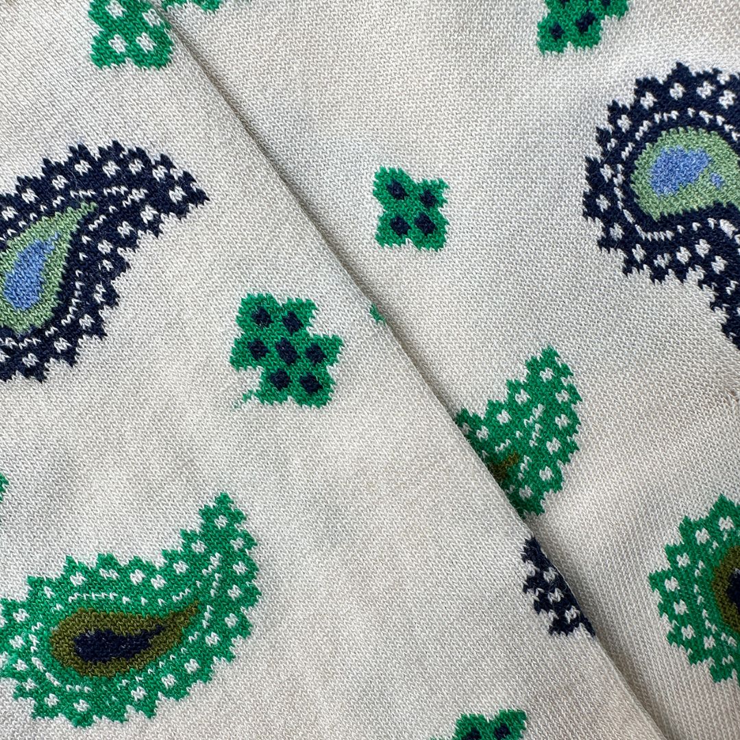 Close-up of socks with a cream base and a repeating paisley and floral pattern in green, navy blue, and light blue.