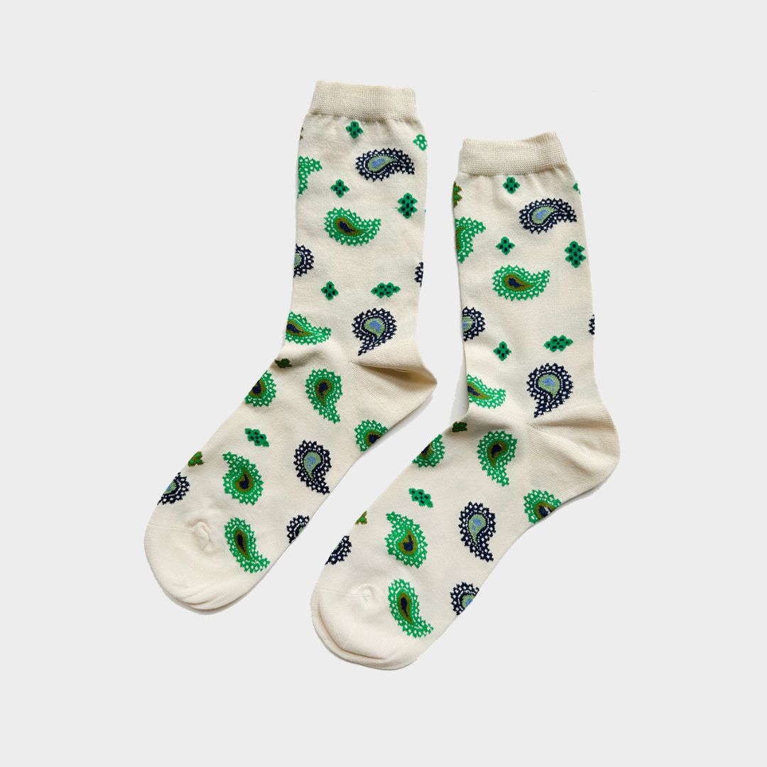 A pair of cream-colored crew socks with a green and dark blue paisley pattern, displayed against a light gray background.