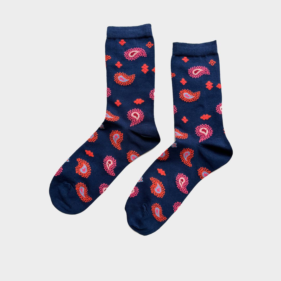 A pair of navy blue crew socks with a vibrant red, pink, and orange paisley pattern, displayed against a light gray background.