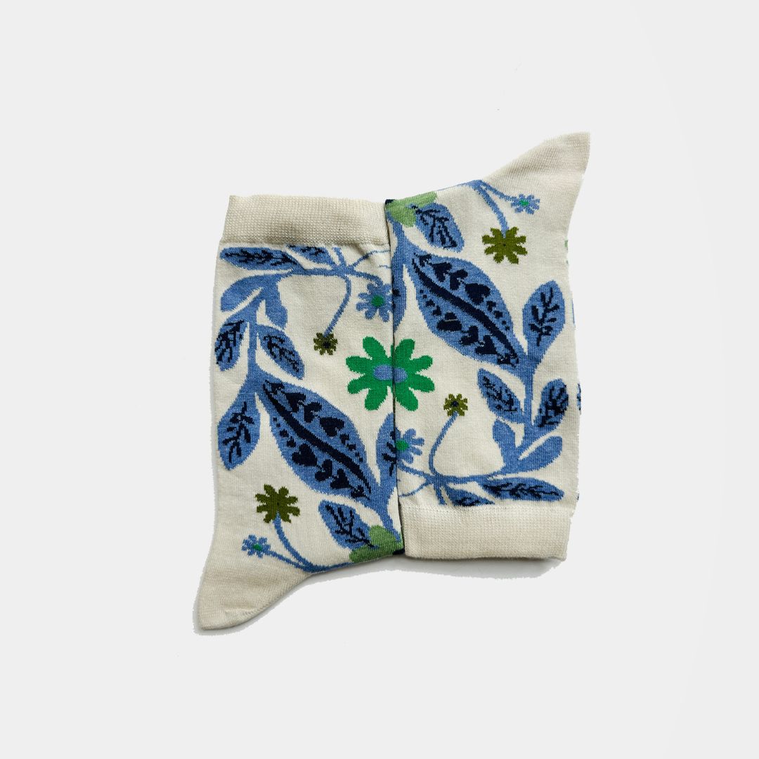 socks with a cream-colored base featuring a blue and green floral and leaf pattern, photographed on a light gray background.