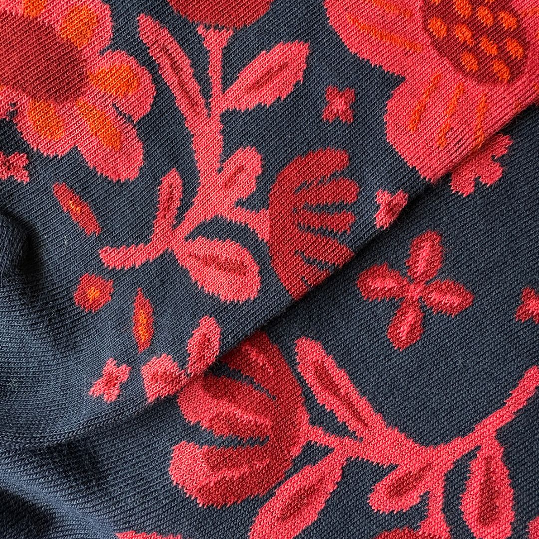 A close-up of socks with a floral pattern in vibrant red and orange on a dark charcoal gray background.