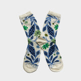 A pair of cream-colored crew socks with a blue and green botanical pattern, displayed in a crossed arrangement against a light gray background.