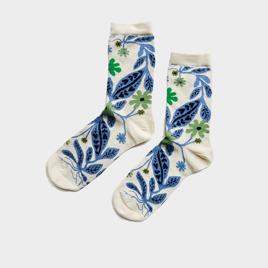A pair of cream-colored crew socks with a blue and green botanical pattern, displayed flat against a light gray background.