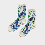 A pair of cream-colored crew socks with a blue and green botanical pattern, displayed flat against a light gray background.