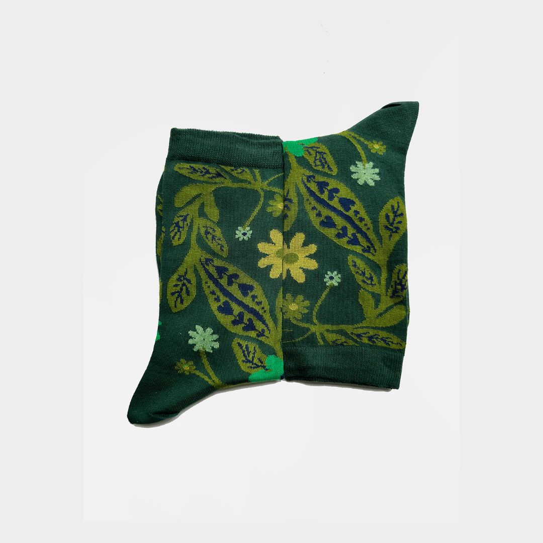 A pair of dark green crew socks with a botanical pattern of yellow, green, and light blue leaves and flowers, displayed against a plain white background.