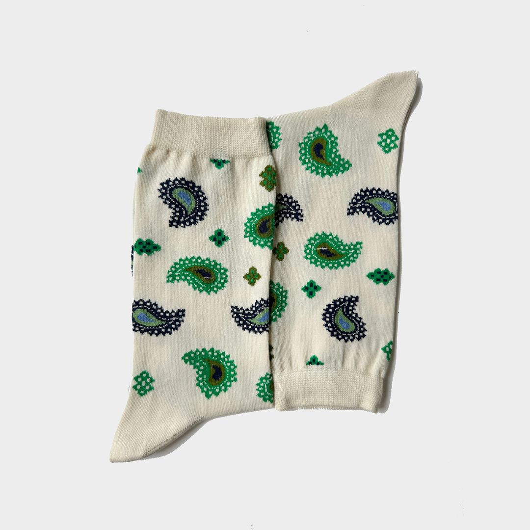 A pair of cream-colored crew socks with a green and black paisley pattern, laid flat against a light gray background.