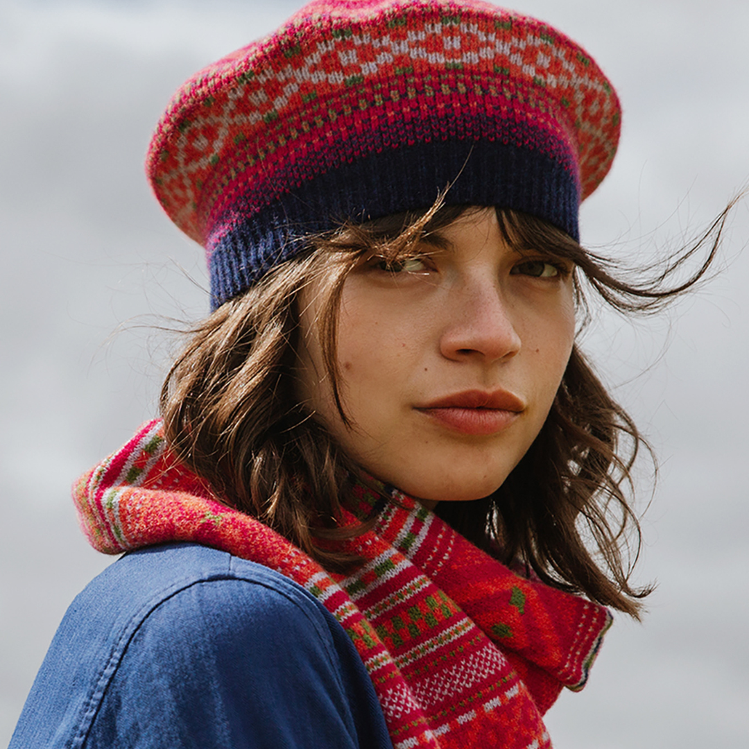 Person wearing a red and blue patterned knit hat and scarf against a neutral background