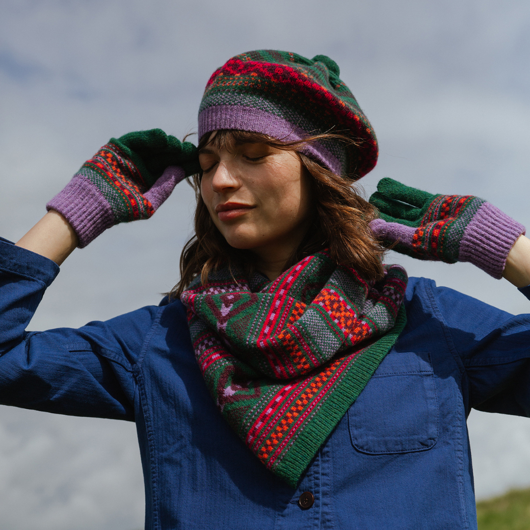 Person wearing a colorful knitted hat, scarf, and gloves against a cloudy sky.