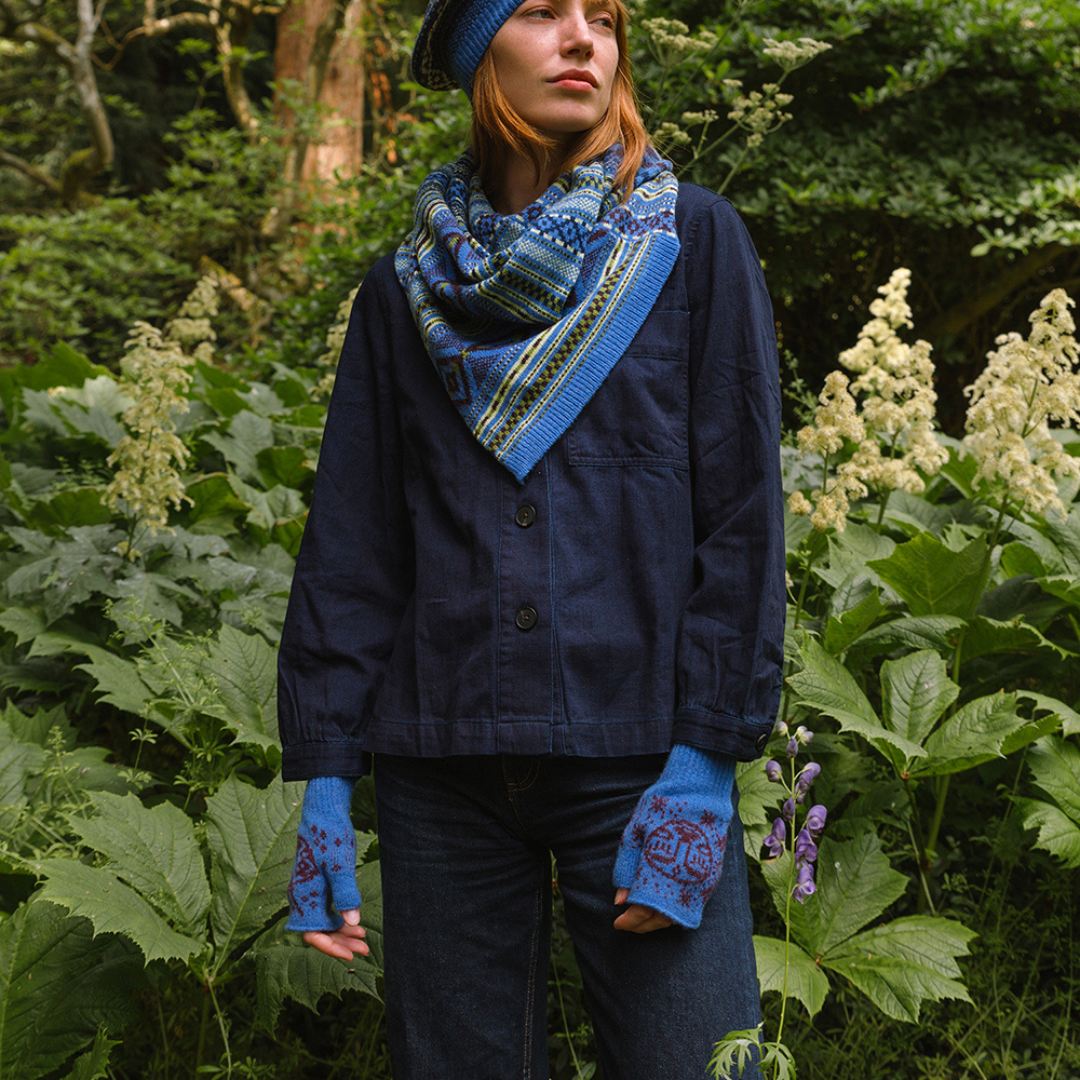 Person wearing a blue jacket, scarf, and gloves standing in a forest setting