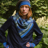 Person wearing a blue knitted hat, scarf, and gloves standing in a garden.