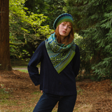 Person wearing a patterned scarf and hat in a forest setting