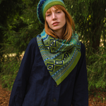 woman wearing a green with blue scarf in a woodland area.