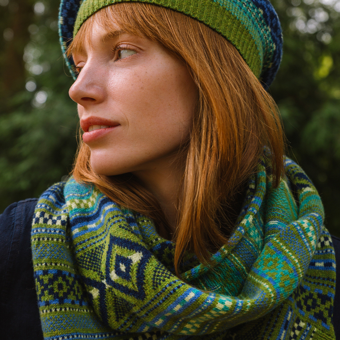 Woman wearing a green and blue patterned hat and scarf against a blurred natural background