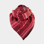 A red patterned knit scarf with geometric and tribal-inspired designs, folded and displayed on a light gray background.
