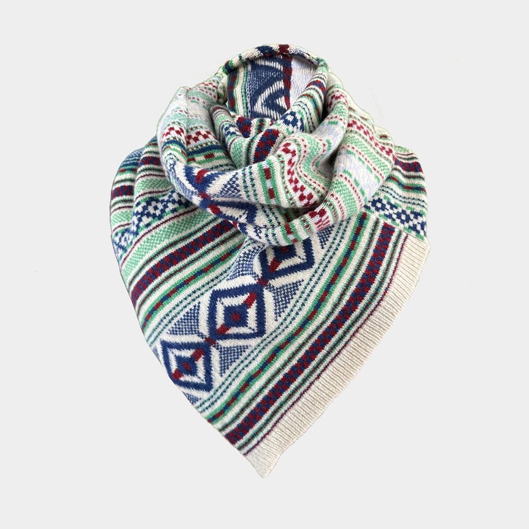 A knitted triangular scarf with a multicolor geometric pattern, featuring navy blue, green, red, and cream stripes and diamond motifs, displayed on a light gray background.