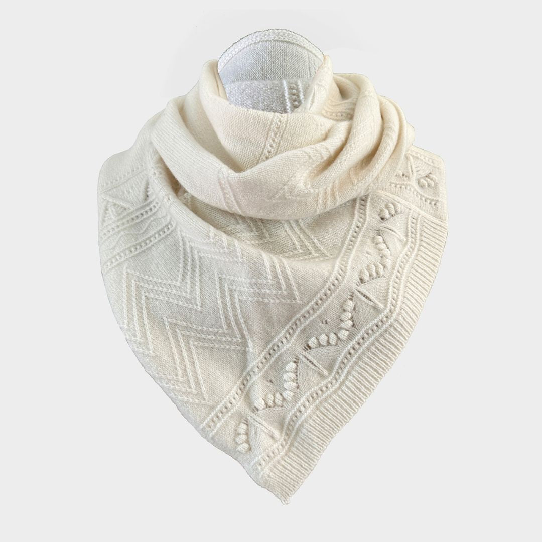 An off-white knit scarf with geometric patterns and pom-pom details, displayed on a mannequin neck against a light gray background.