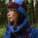 Person wearing a blue and purple knit hat and scarf in a forest setting