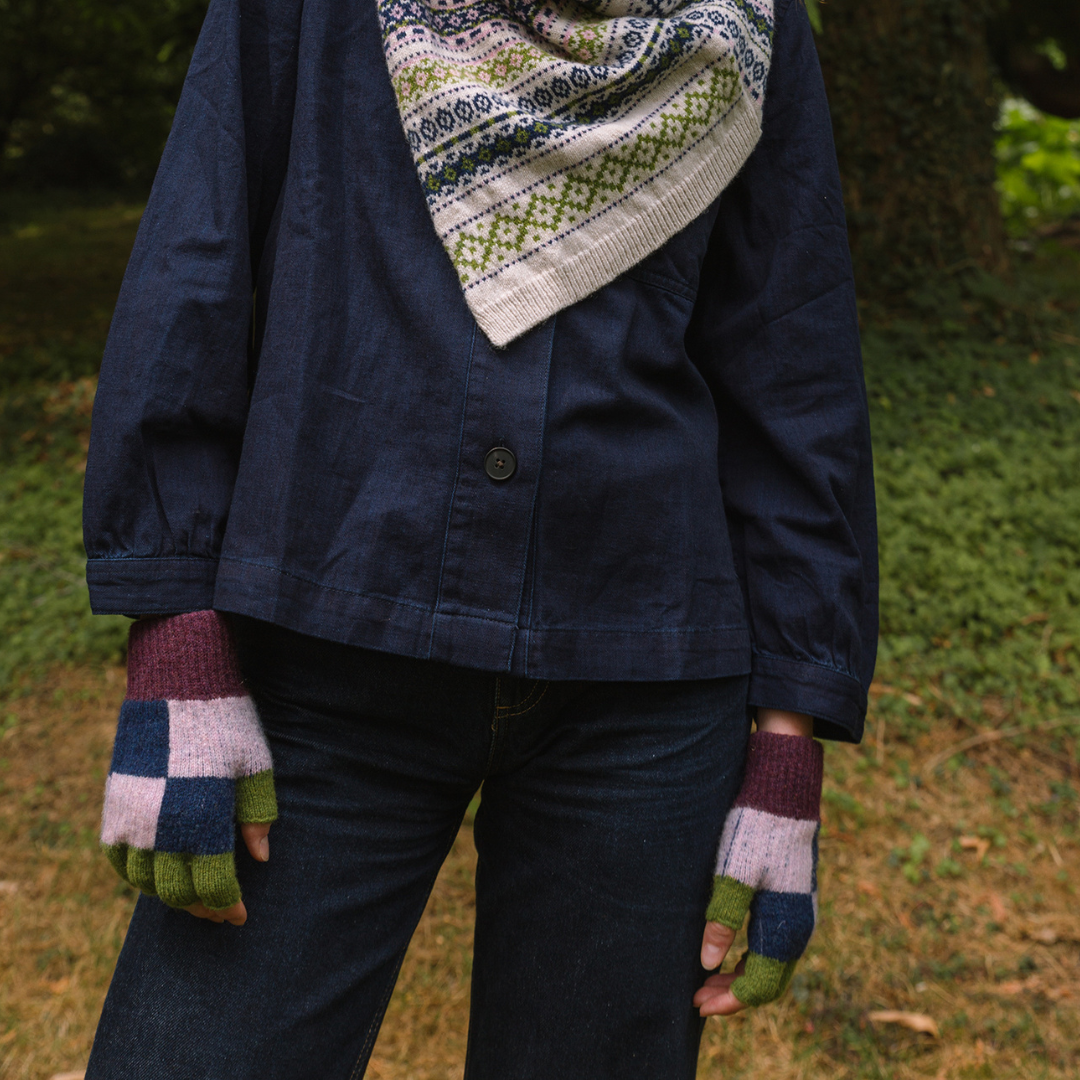 Person wearing a navy jacket, patterned scarf, and checkered gloves standing outdoors.