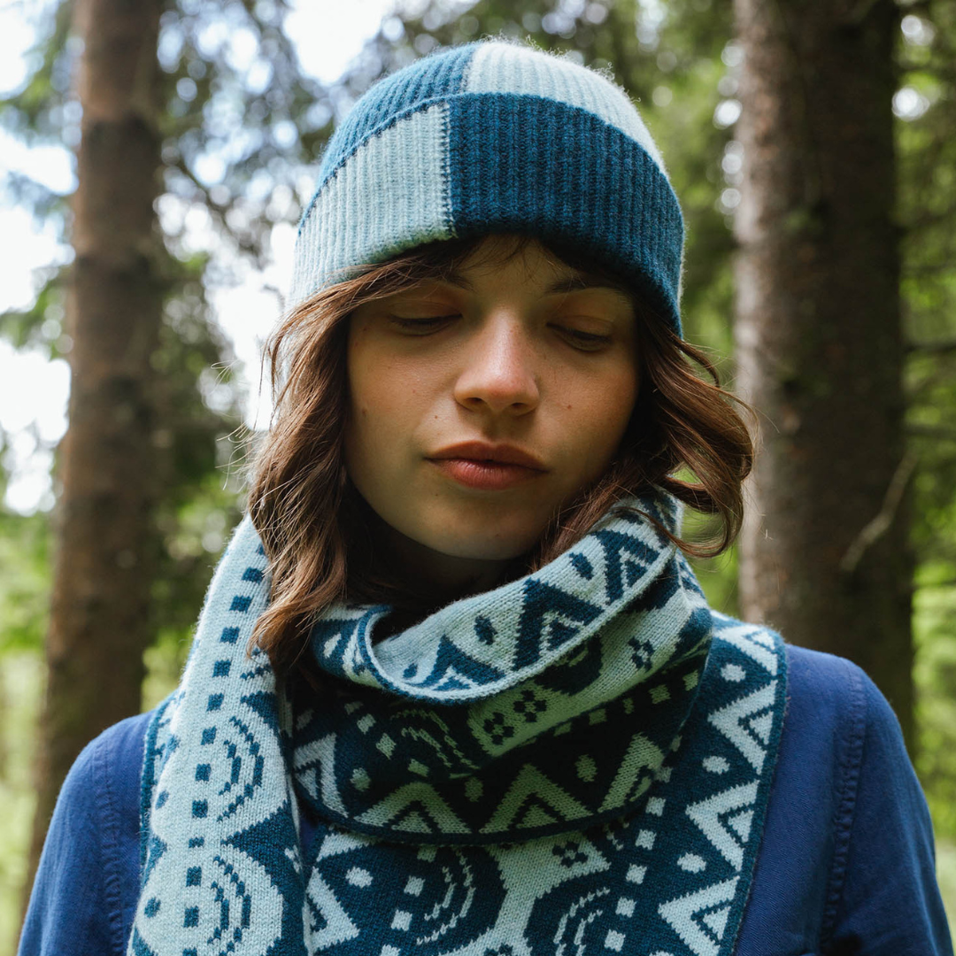 Person wearing a blue and white patterned knit hat and scarf in a forest setting