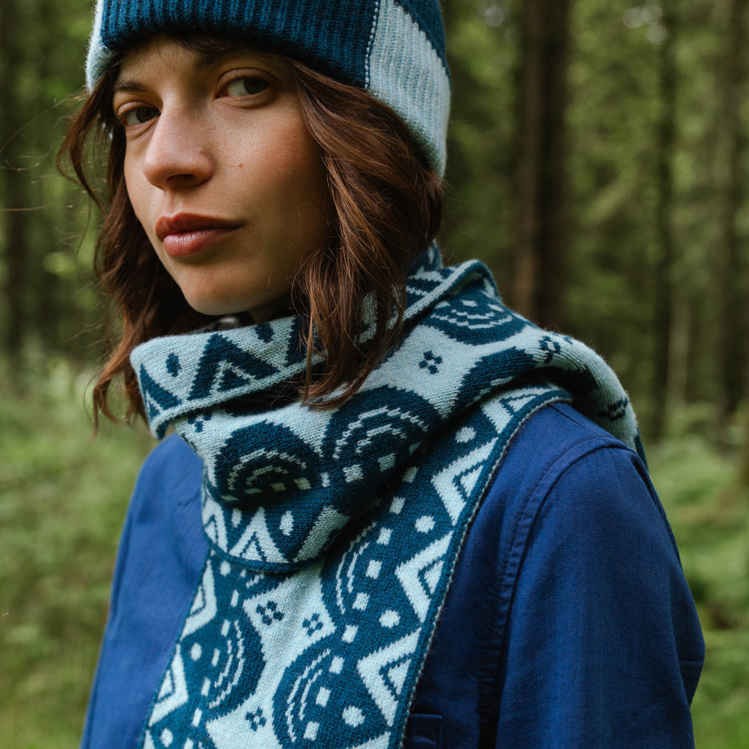 Person wearing a blue and white patterned scarf and hat in a forest setting