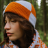 Woman wearing an orange and gray knit hat and scarf in a forest setting