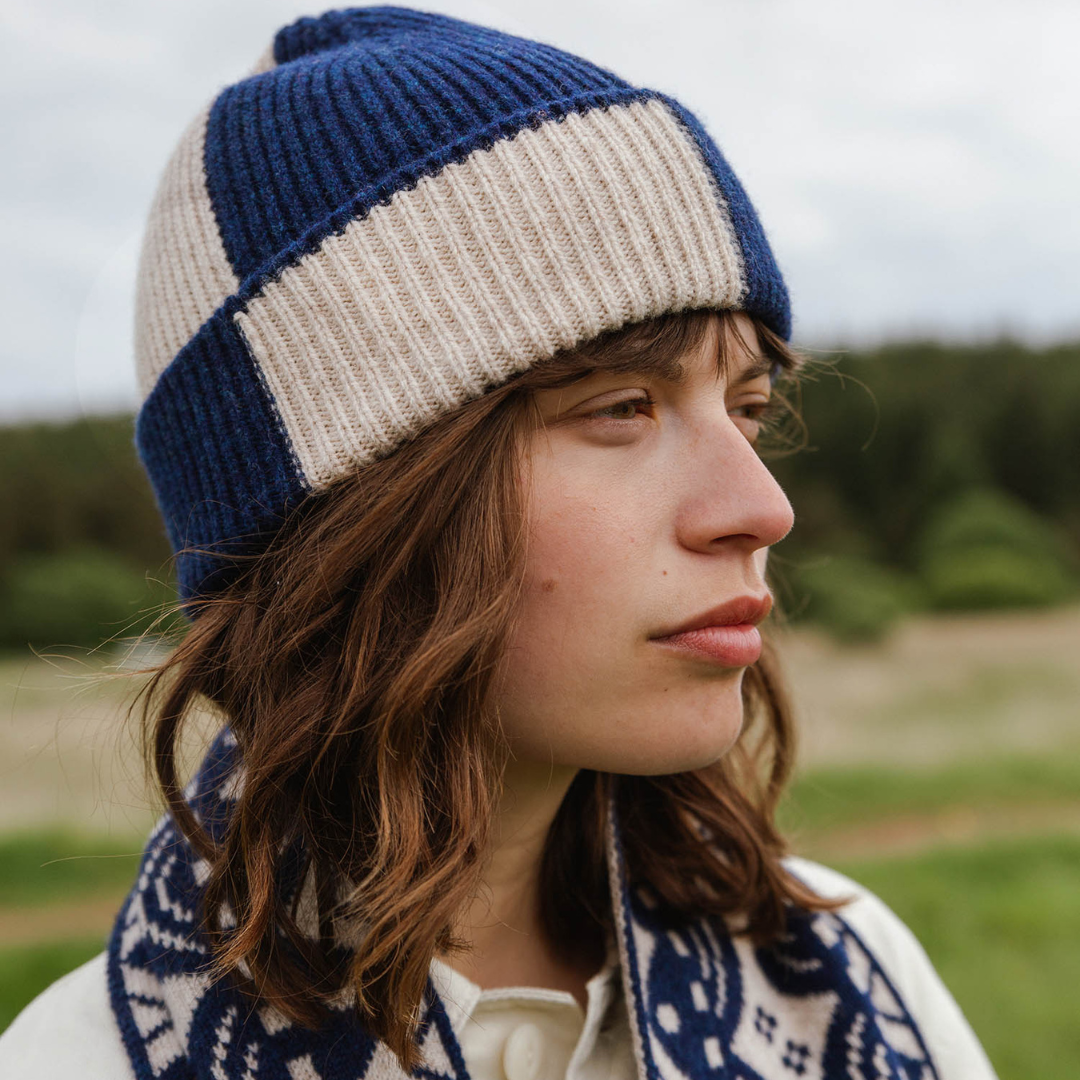 Person wearing a blue and beige striped knit hat with a patterned scarf outdoors.
