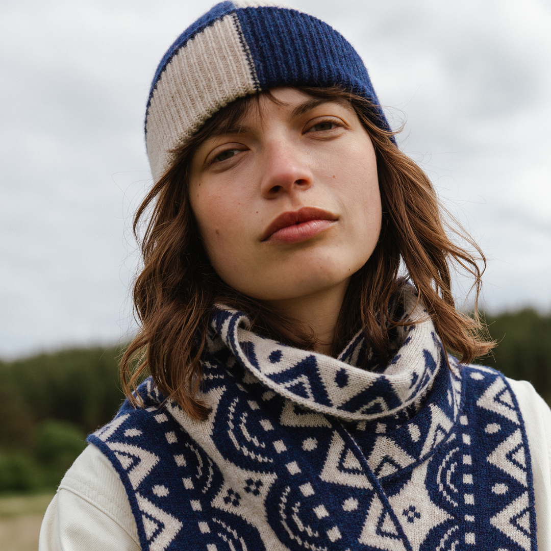 Person wearing a blue and beige knit hat and a patterned scarf outdoors.